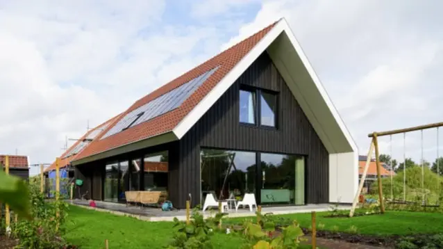 Foto van schuurwoning met een houten zwarte gevel met rode dakpannen, grote ramen en zonnepanelen
