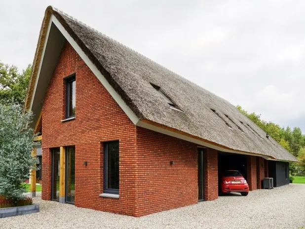 Foto van een schuurwoning met rode bakstenen en een rieten kap