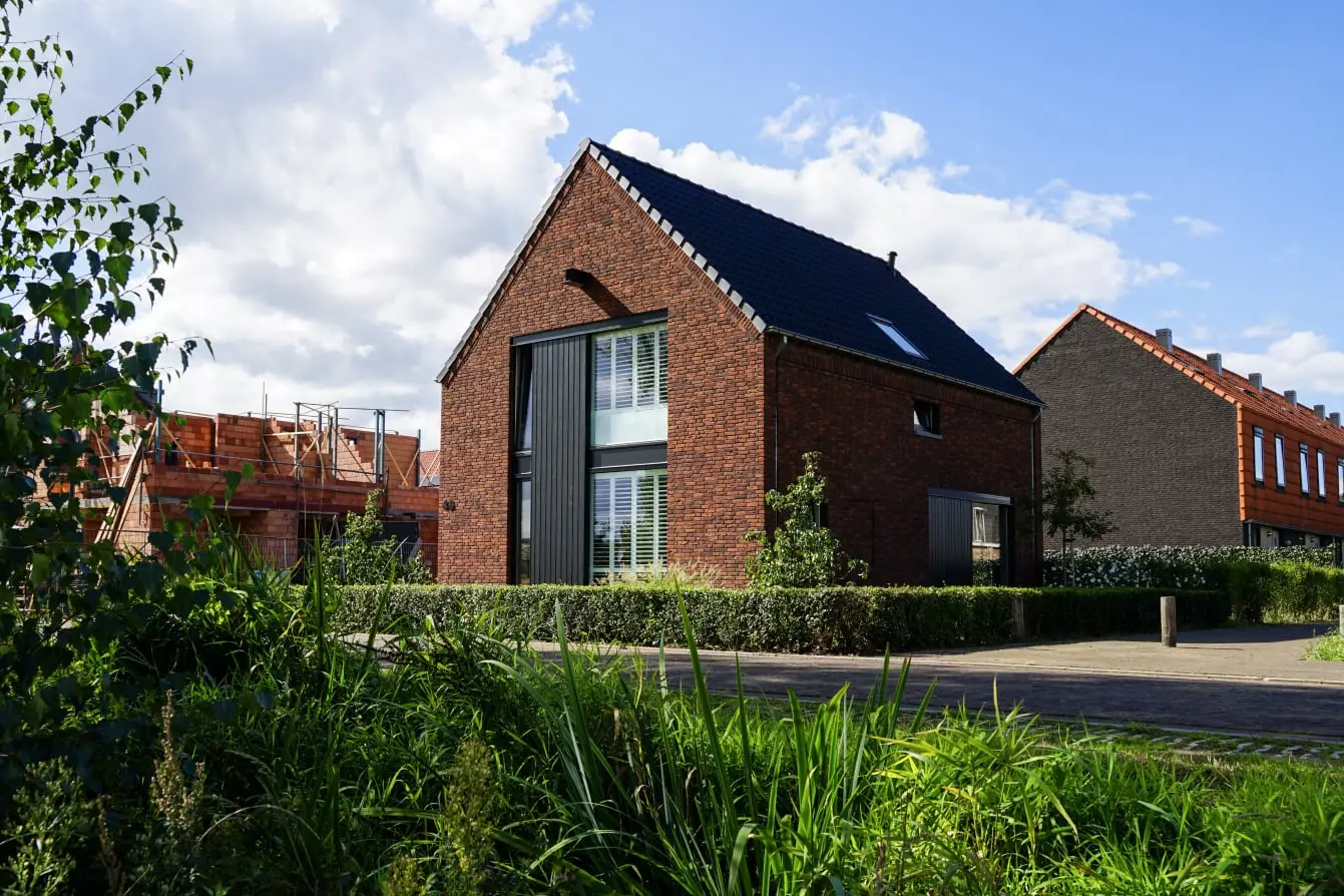 Foto van een Smidse woning in industriële stijl met rode bakstenen en vlakke dakpannen. Grote ramen aan de voorkant en een zadeldak.