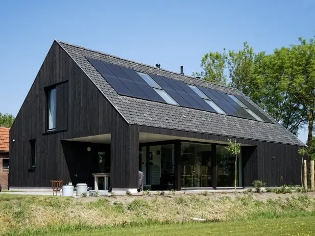 Foto van een moderne schuurwoning met een zwarte houten gevel, grote raampartijen en zwarte dakpannen.