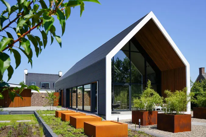 Foto van een moderne schuurwoning met oranje dakpannen, een zwarte houten gevel en veel lichtinval